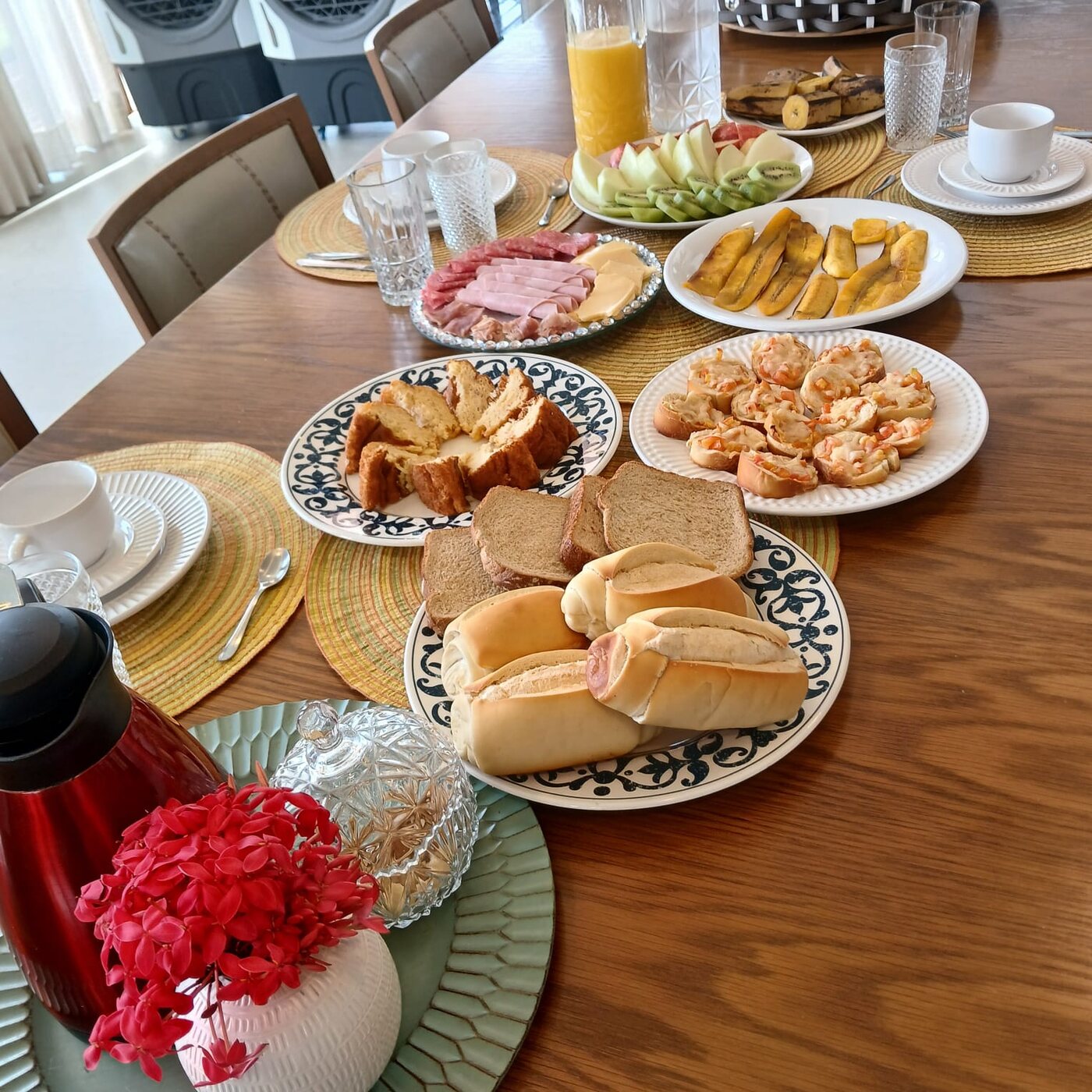 Mesa de café da manhã com pães, frutas, frios e bebidas
