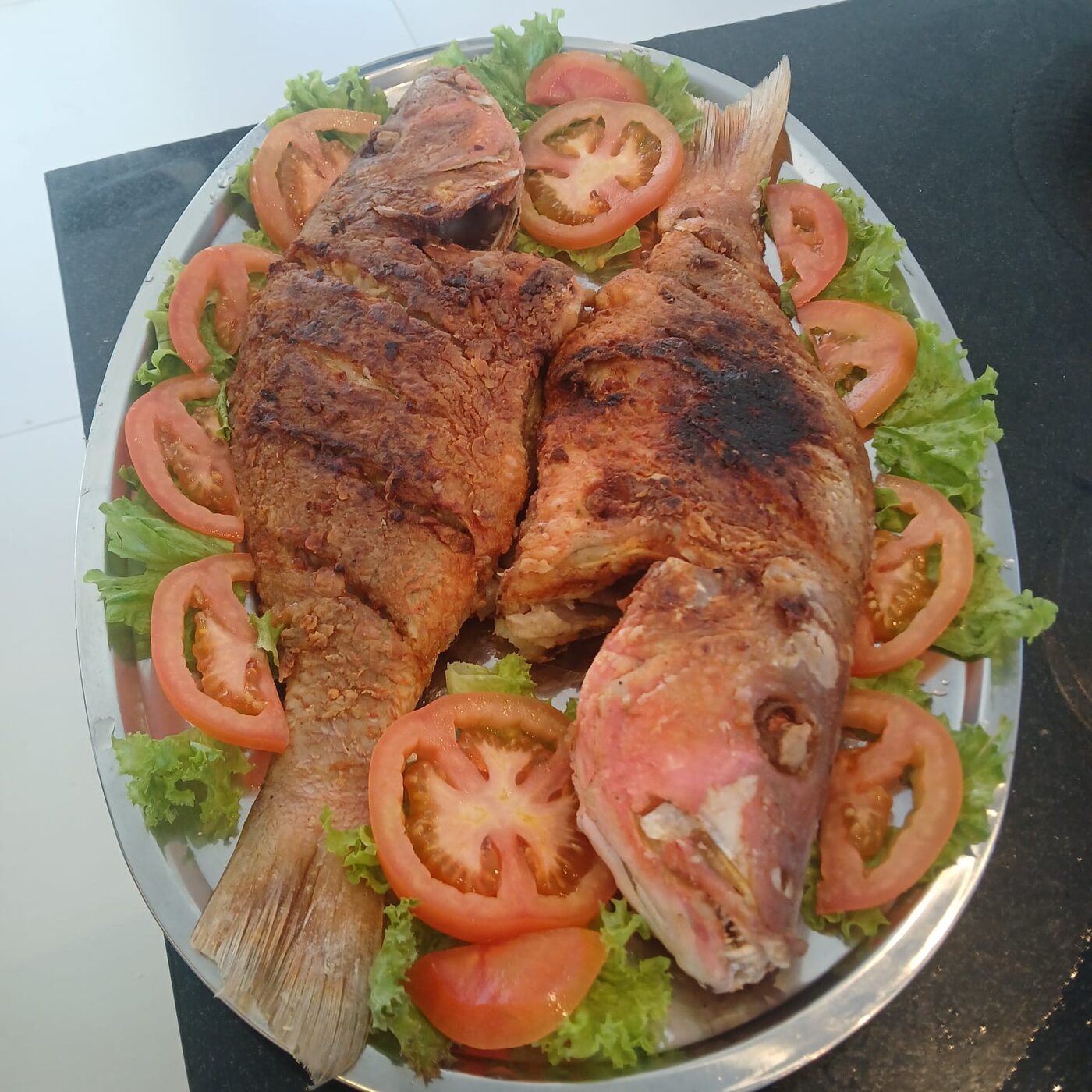 Peixes assados servidos sobre folhas e tomates